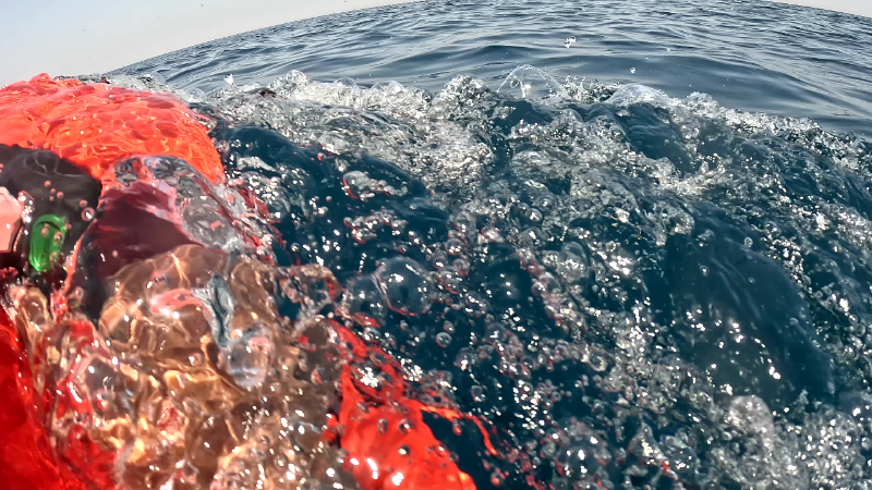 Point-of-view shot of a swimmer holding a motorised sea scooter at the ocean surface near a boat