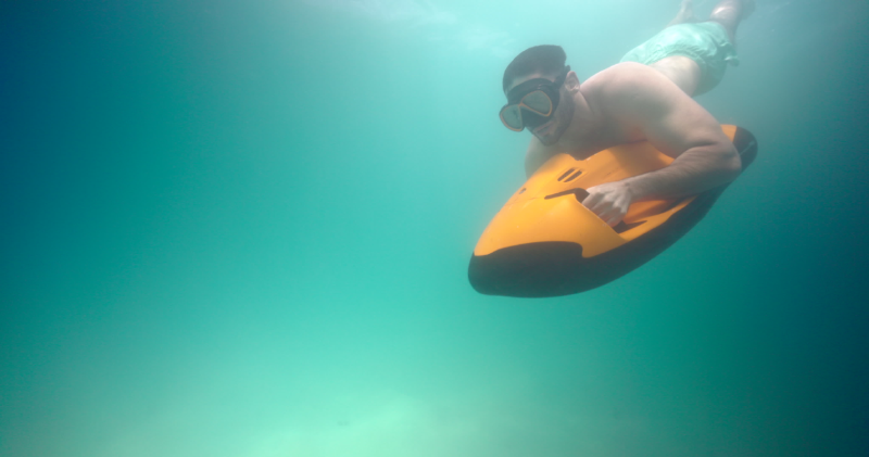 A swimmer holds on to a motorised sea scooter while swimming underwater