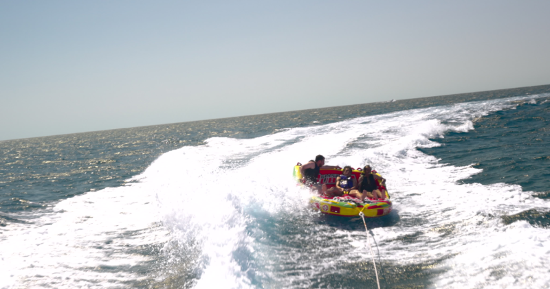 People riding an inflatable towable tube behind a boat on open ocean waters
