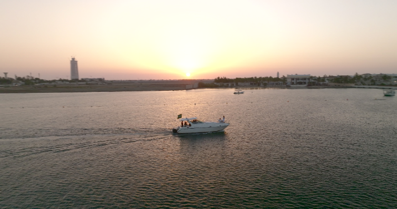 Aerial view of a boat cruising across calm water at sunset with the coastline in the background